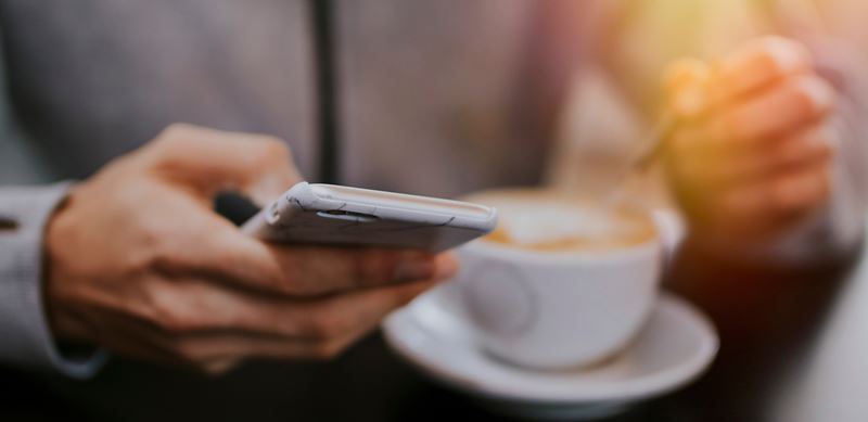 person holding cell phone with cup of coffee